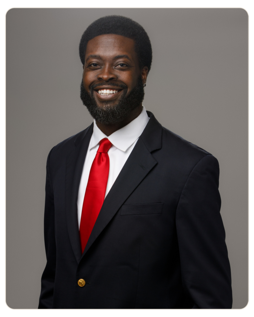 Ahmad Bryant Chief Executive Officer Smiling man in a dark suit and red tie against a gray backdrop