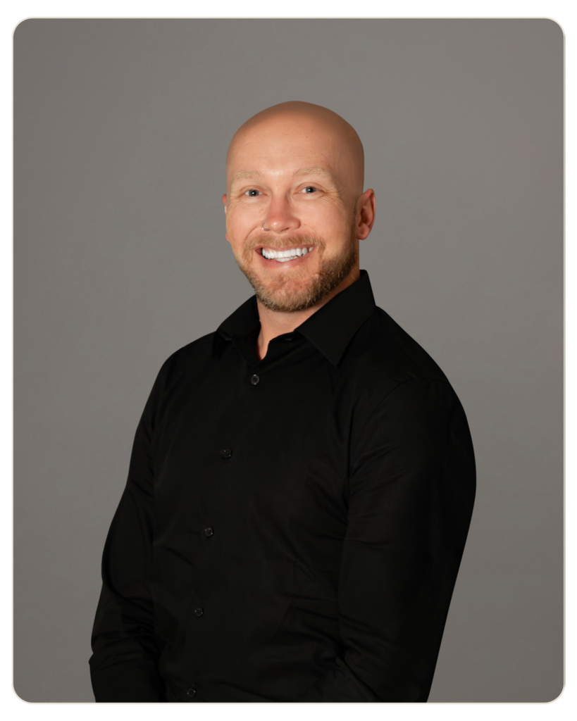Smiling bald man in a black shirt against a gray studio backdrop.