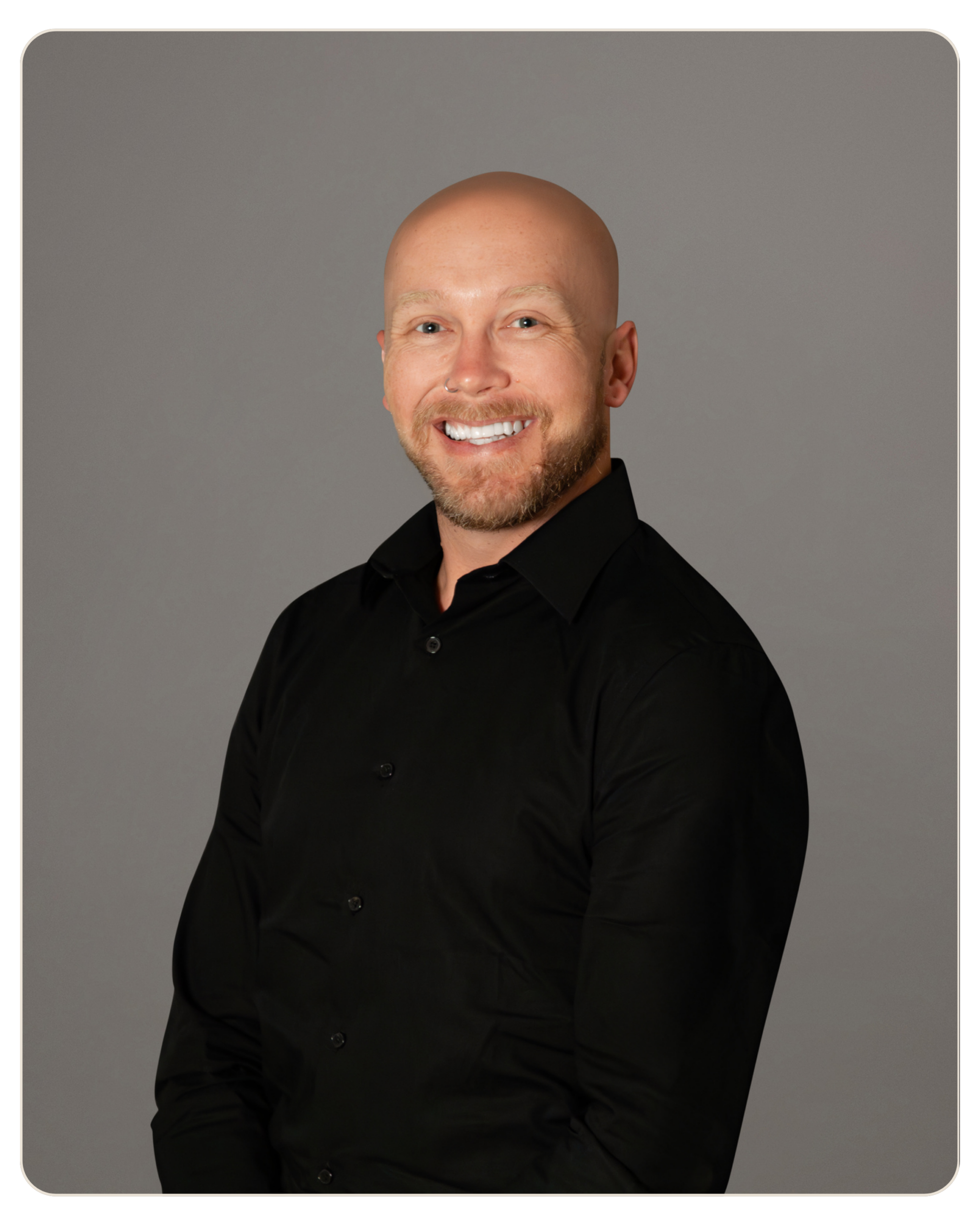 Smiling bald man in a black shirt against a gray studio backdrop.