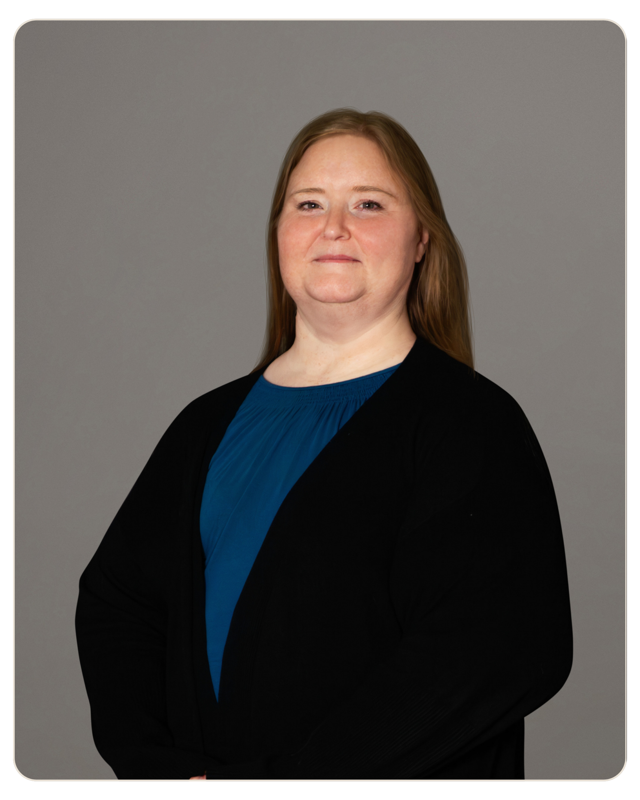 Jodie Simpson, LMFT Portrait of a smiling woman with light brown hair wearing a blue top and black blazer against a gray backdrop, arms crossed lightly to the side.