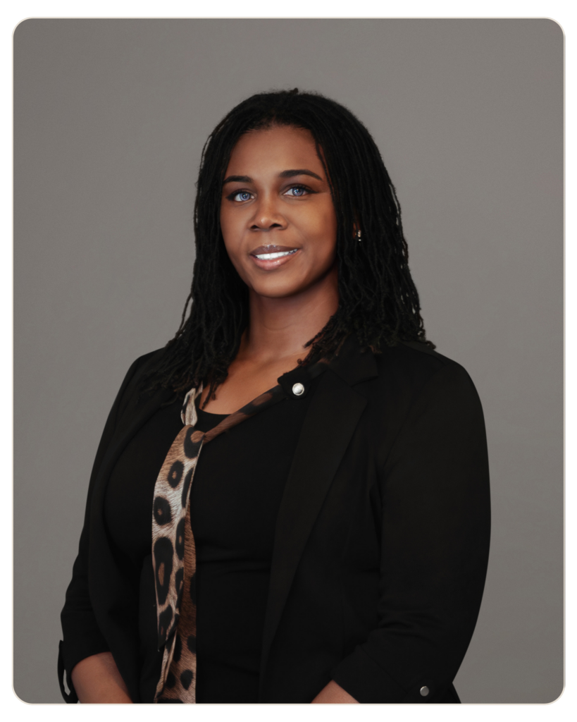 Kizzy Thomas, MSW Primary Therapist Head-and-shoulders portrait of a smiling African American woman with braided hair, wearing a black blazer and leopard scarf, gray background.
