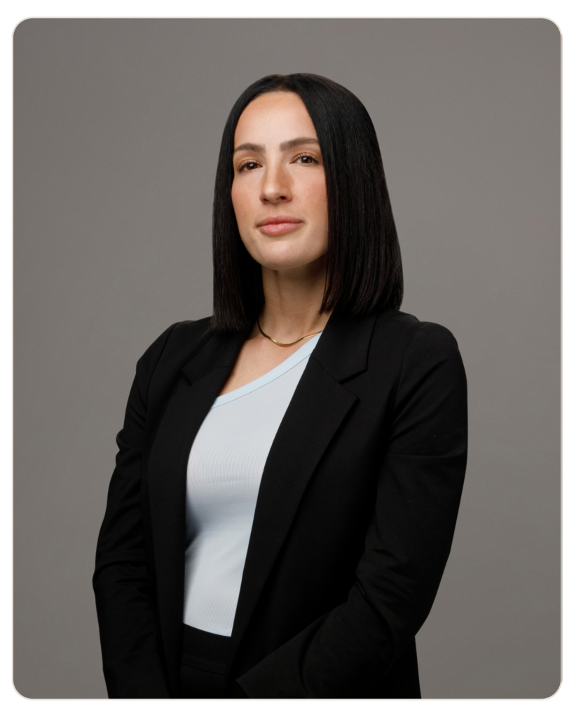 Flyland Maryann Ricci Professional head-and-shoulders portrait of a woman with straight black hair, wearing a black blazer over a light blue top, neutral gray background.