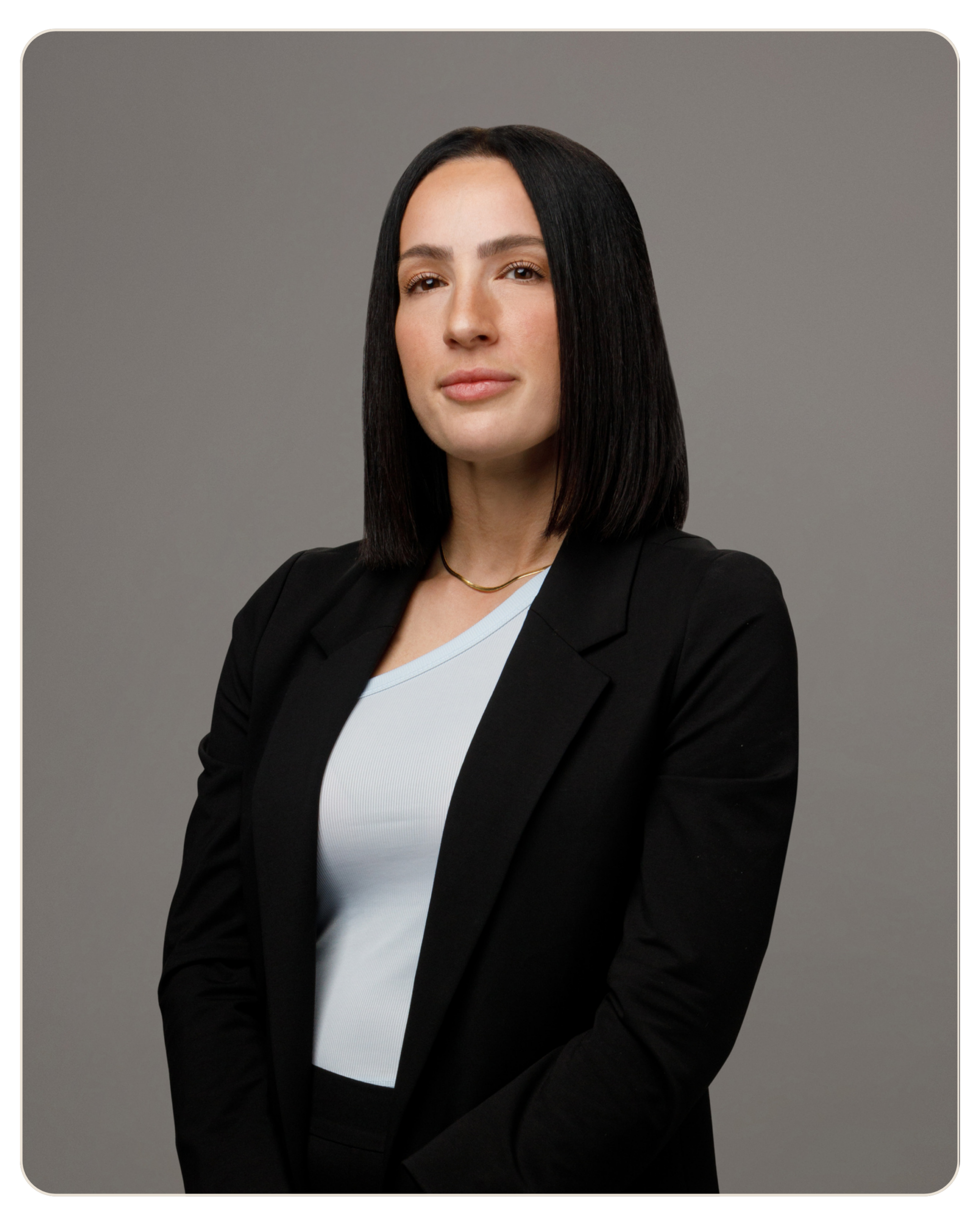 Flyland Maryann Ricci Professional head-and-shoulders portrait of a woman with straight black hair, wearing a black blazer over a light blue top, neutral gray background.