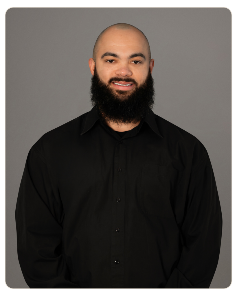 Head-and-shoulders portrait of a bald man with a full beard wearing a black button-down shirt against a gray backdrop.