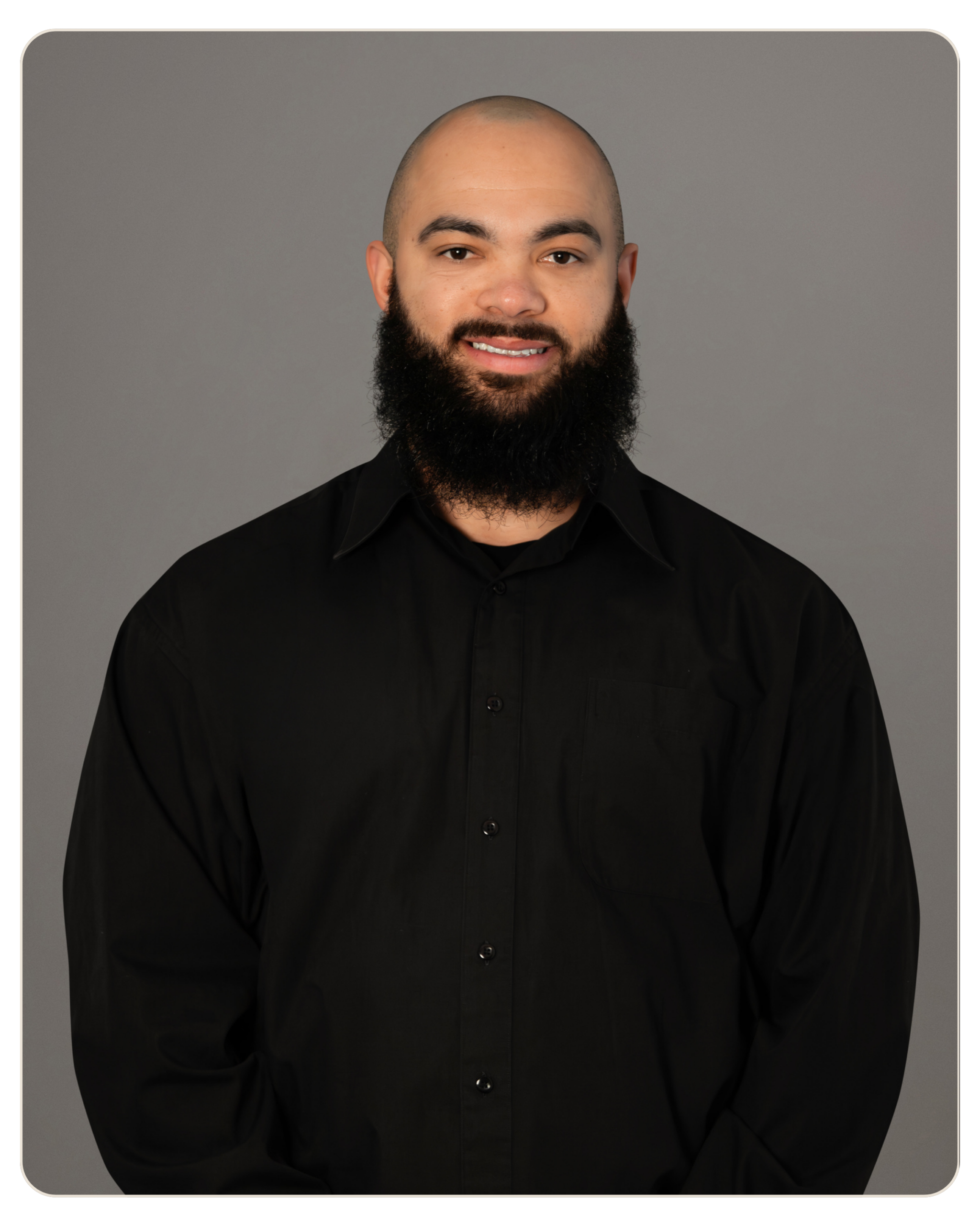 Head-and-shoulders portrait of a bald man with a full beard wearing a black button-down shirt against a gray backdrop.